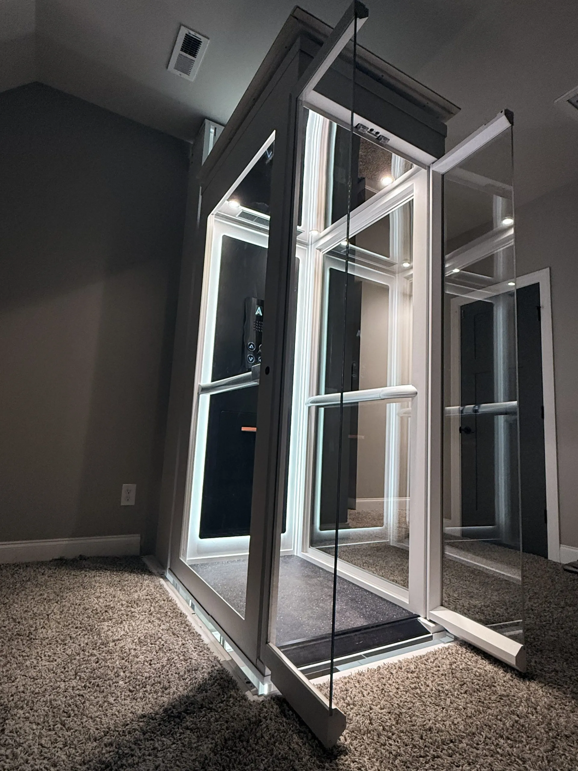 Ascenda Size M home lift dengan pintu kaca terbuka, instalasi indoor di rumah dua lantai, pencahayaan kabin terlihat jelas