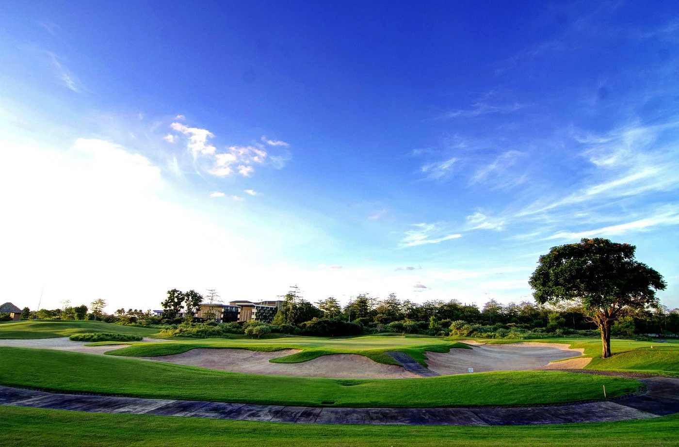 Panorama lapangan New Kuta Golf Bali dengan fairway luas, bunker, dan langit biru menjelang sore.