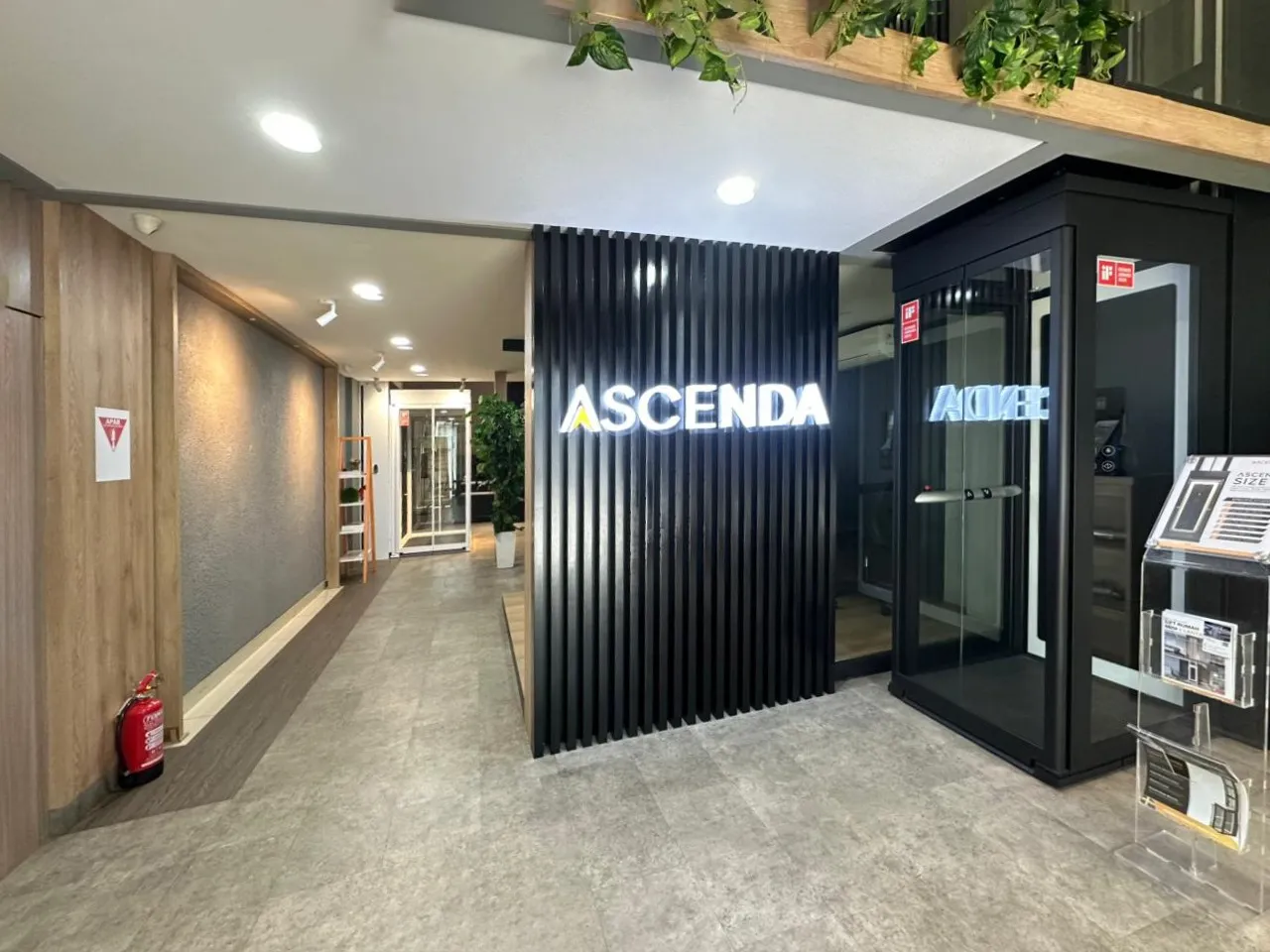 Area showroom Ascenda dengan signage “ASCENDA”, unit lift display di sisi kanan, dan koridor showroom yang rapi.